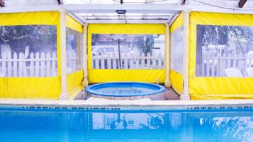 Piscina techada con valla amarilla y blanca, un jacuzzi y vista a una cerca blanca de piquete y coches estacionados.