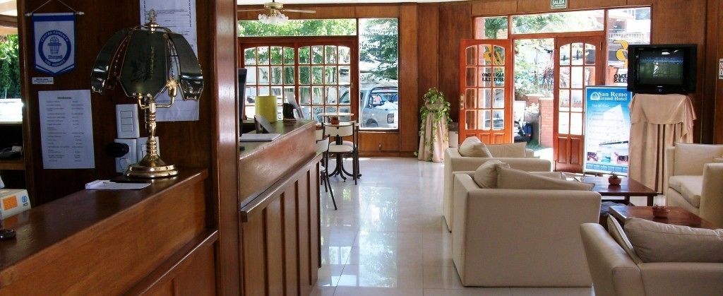 Uma área de recepção com uma mesa de madeira, uma luminária, uma televisão e um espaço de estar com sofás.