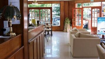 Uma área de recepção com uma mesa de madeira, uma luminária, uma televisão e um espaço de estar com sofás.