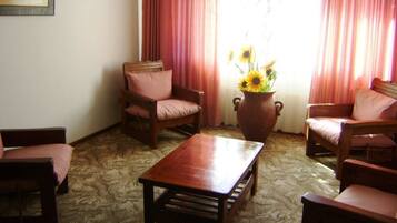 Una habitación con una mesa de centro de madera, dos sillones, un sofá y un jarrón grande con girasoles.
