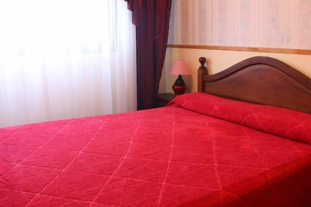 Una cama con colcha roja, cabecera de madera y dos lámparas de noche.