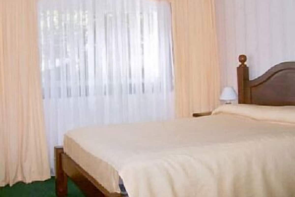 Un dormitorio con una cama de madera, cortinas blancas y una mesita de noche con lámpara.