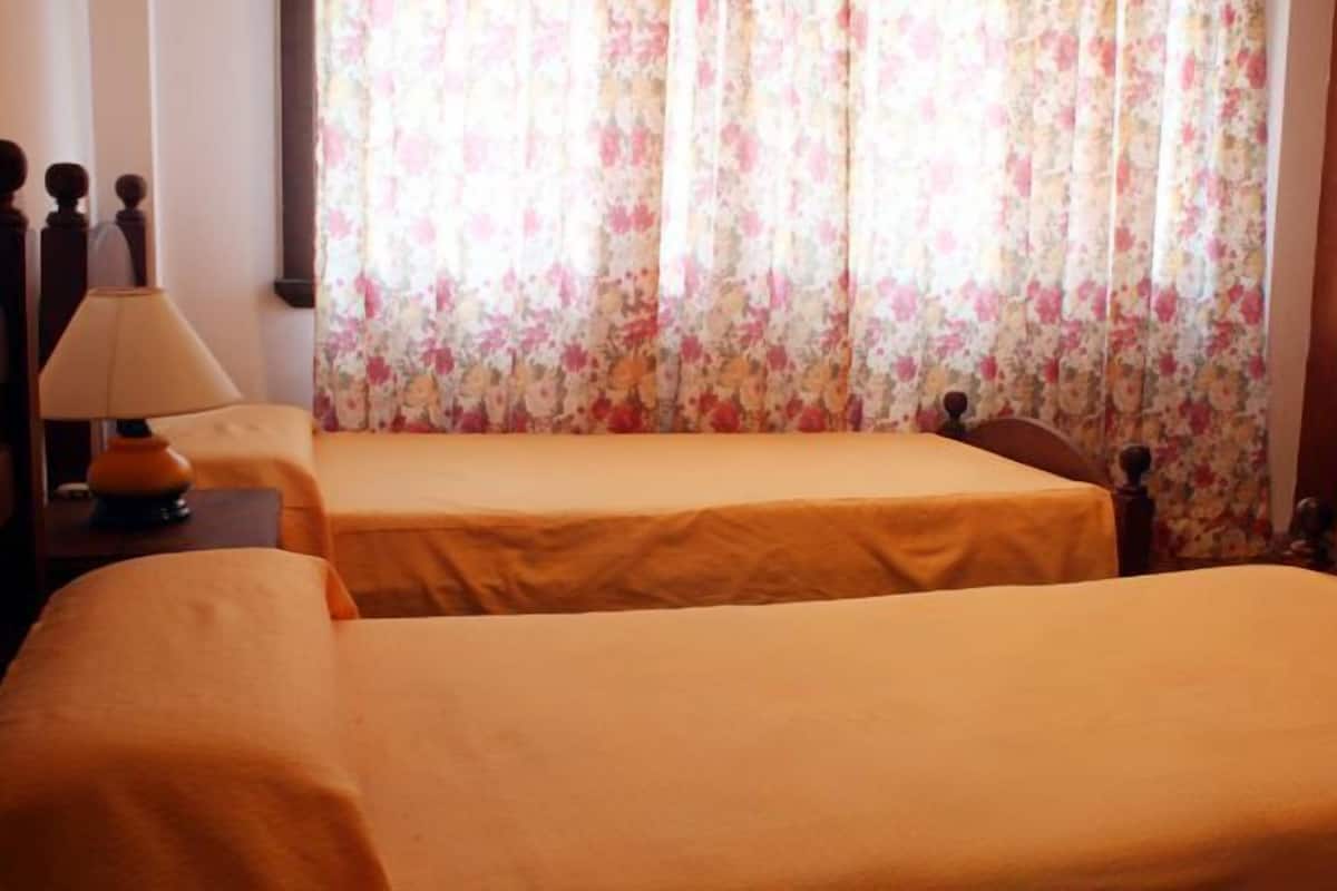 Una habitación de hotel con dos camas individuales, una mesita de noche con lámpara y cortina estampada con motivos florales.