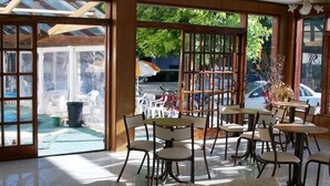 Un'area pranzo interna illuminata dal sole con ampie finestre, una piscina visibile all'esterno e posti a sedere all'aperto.