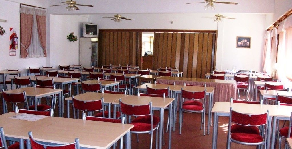 A classroom with rows of desks and chairs, ceiling fans, and a large window.