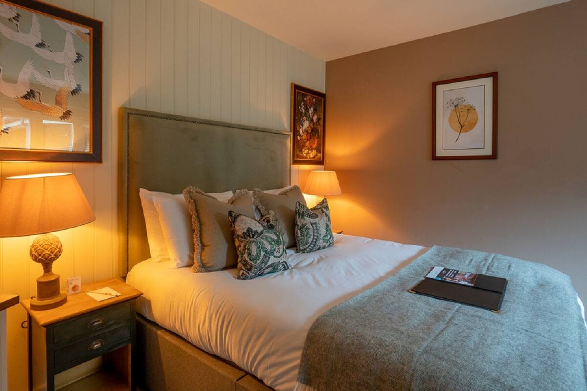 A neatly made bed with multiple pillows, a bedside lamp, and a framed picture on the wall.