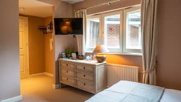 A bedroom with a bed, a dresser, a television mounted on the wall, and a window with curtains.