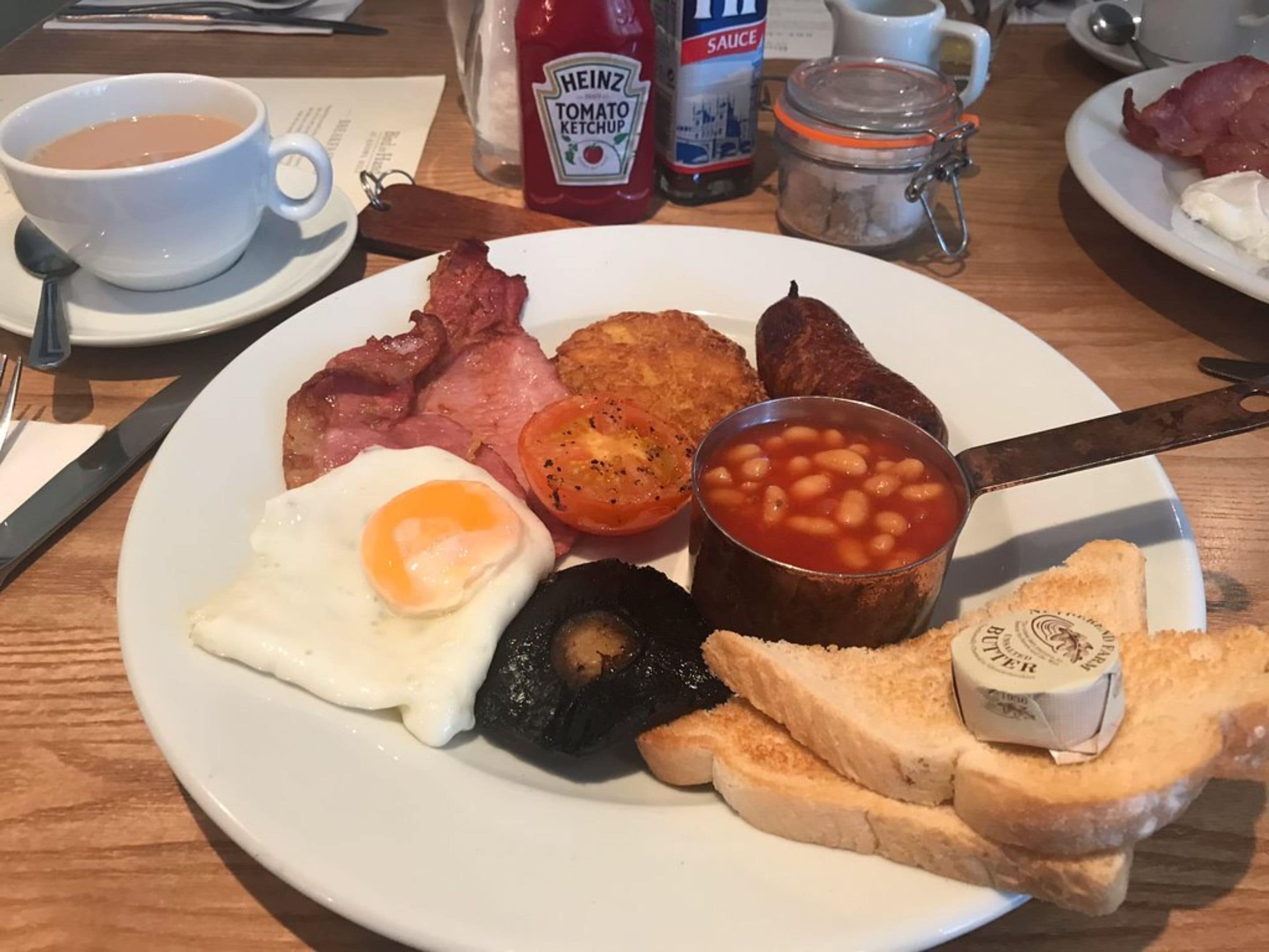 A breakfast plate with bacon, eggs, beans, toast, and a small container of butter.