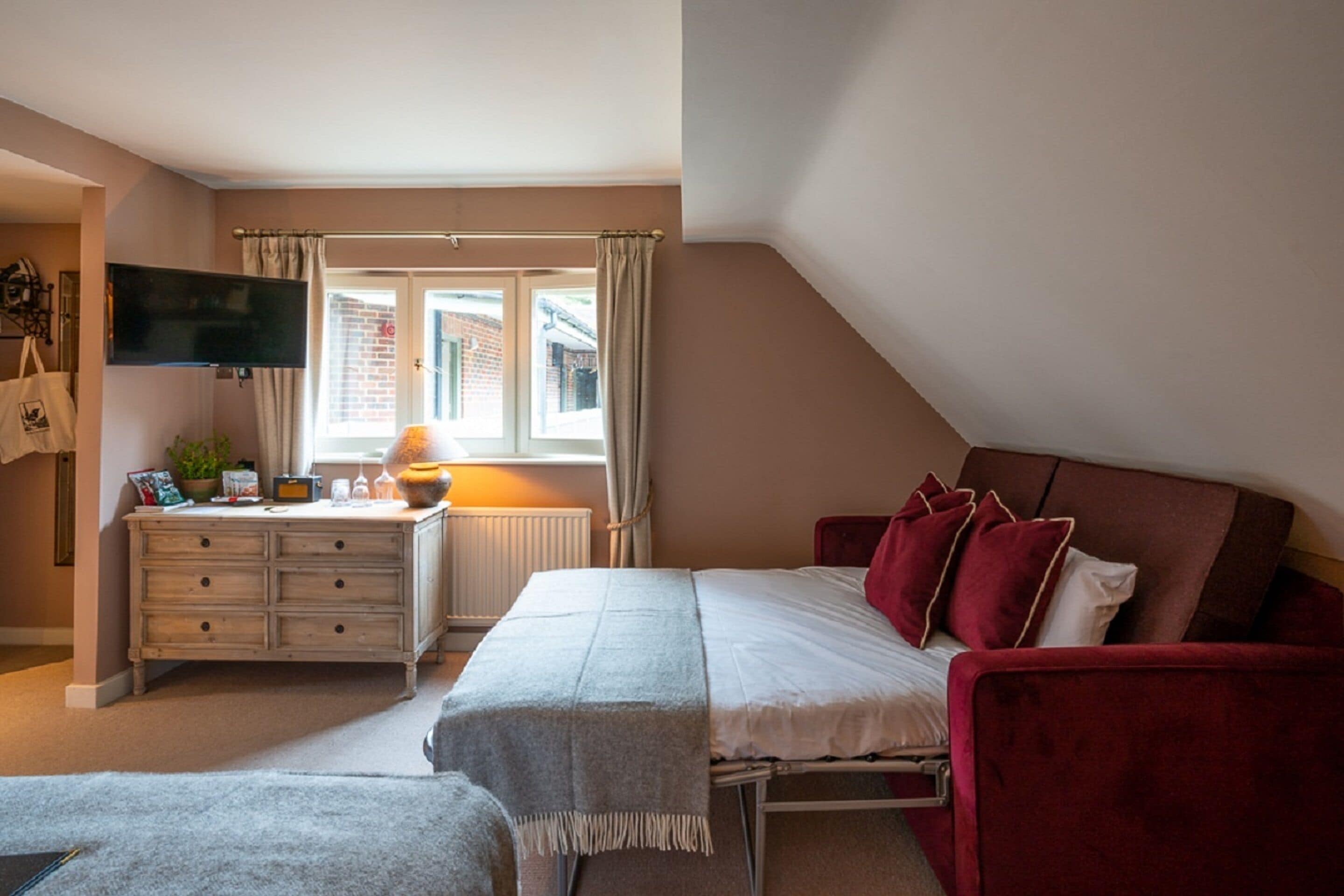 Un dormitorio con cama, escritorio, televisor y ventana con cortinas.