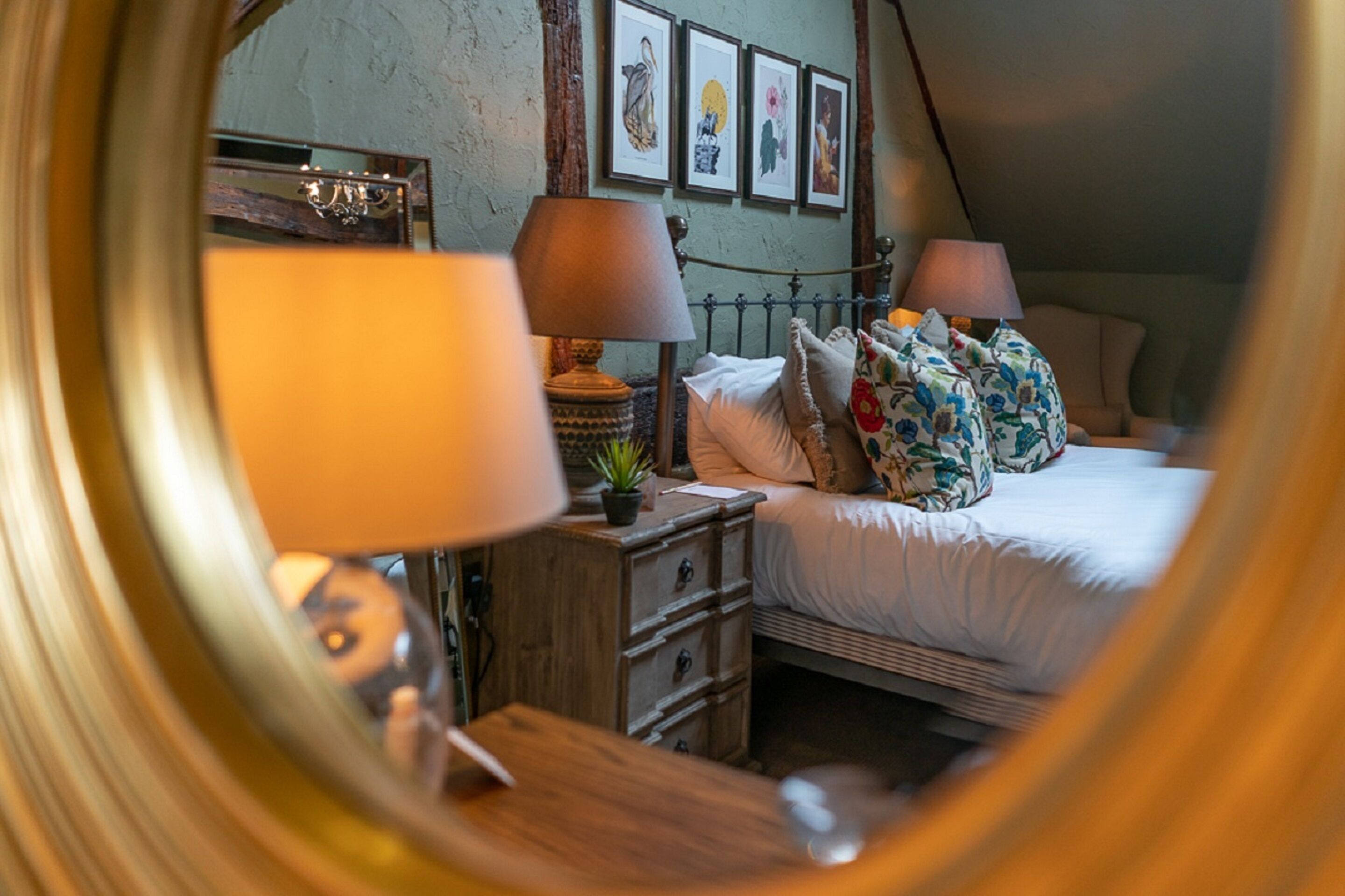 A bedroom with a bed, two bedside tables, a mirror, and a wall with framed artwork.