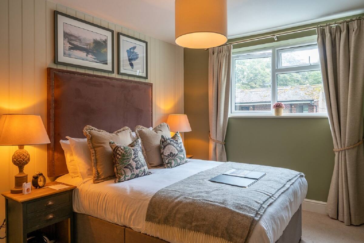 A neatly made bed with a headboard, two bedside lamps, and a window with curtains.