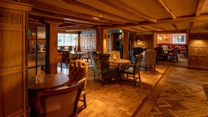 A wooden interior with a herringbone floor, multiple dining tables, and chairs.