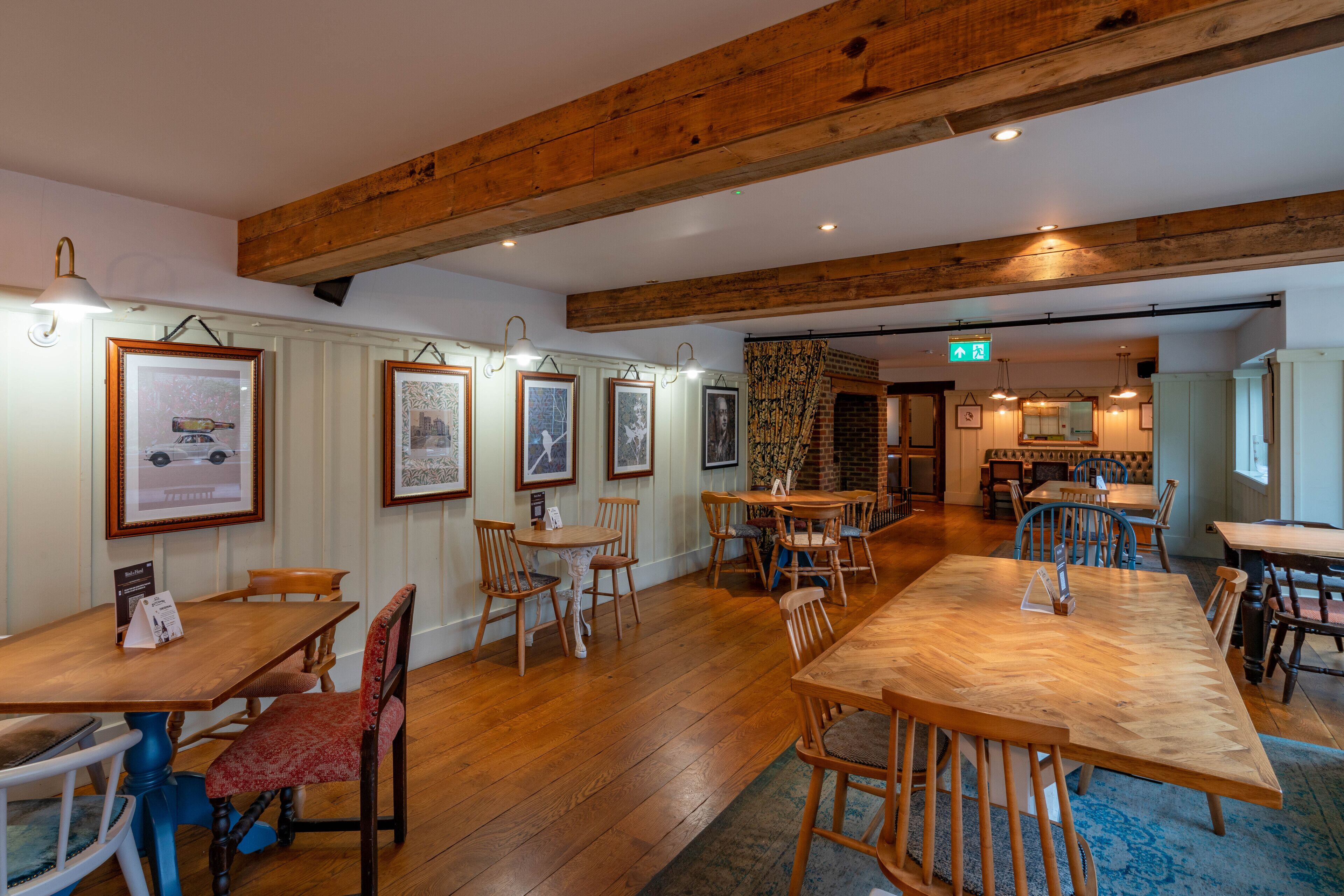 Ein Restaurant mit Holztischen und -stühlen, gerahmten Bildern an den Wänden und einer Ziegelwand im Hintergrund.