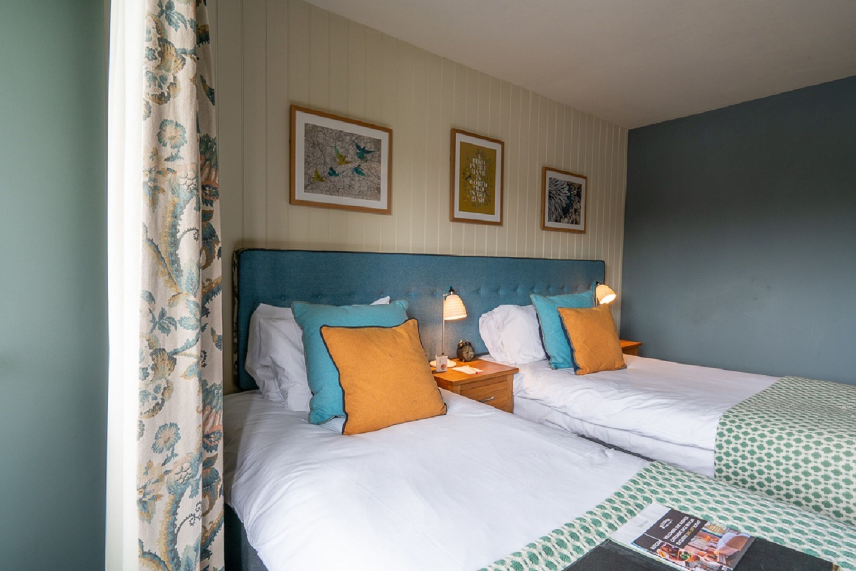 A double bed with white linens, two pillows, a nightstand with a lamp, and a framed picture on the wall.