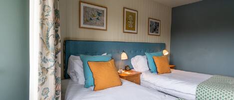 A double bed with white linens, two pillows, a nightstand with a lamp, and a framed picture on the wall.