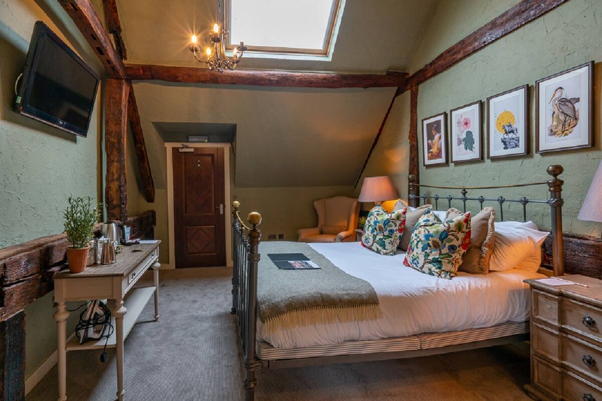 A bedroom with a bed, bedside tables, a desk, a television, and artwork on the wall.