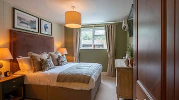 Une chambre avec un grand lit, des lampes de chevet, une table de chevet en bois, une commode en bois, une fenêtre avec des rideaux et des tableaux encadrés accrochés au mur.