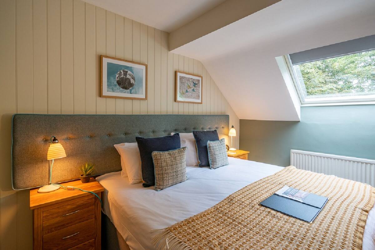 A bedroom with a large bed, a headboard, a bedside table with a lamp, and two framed pictures on the wall.