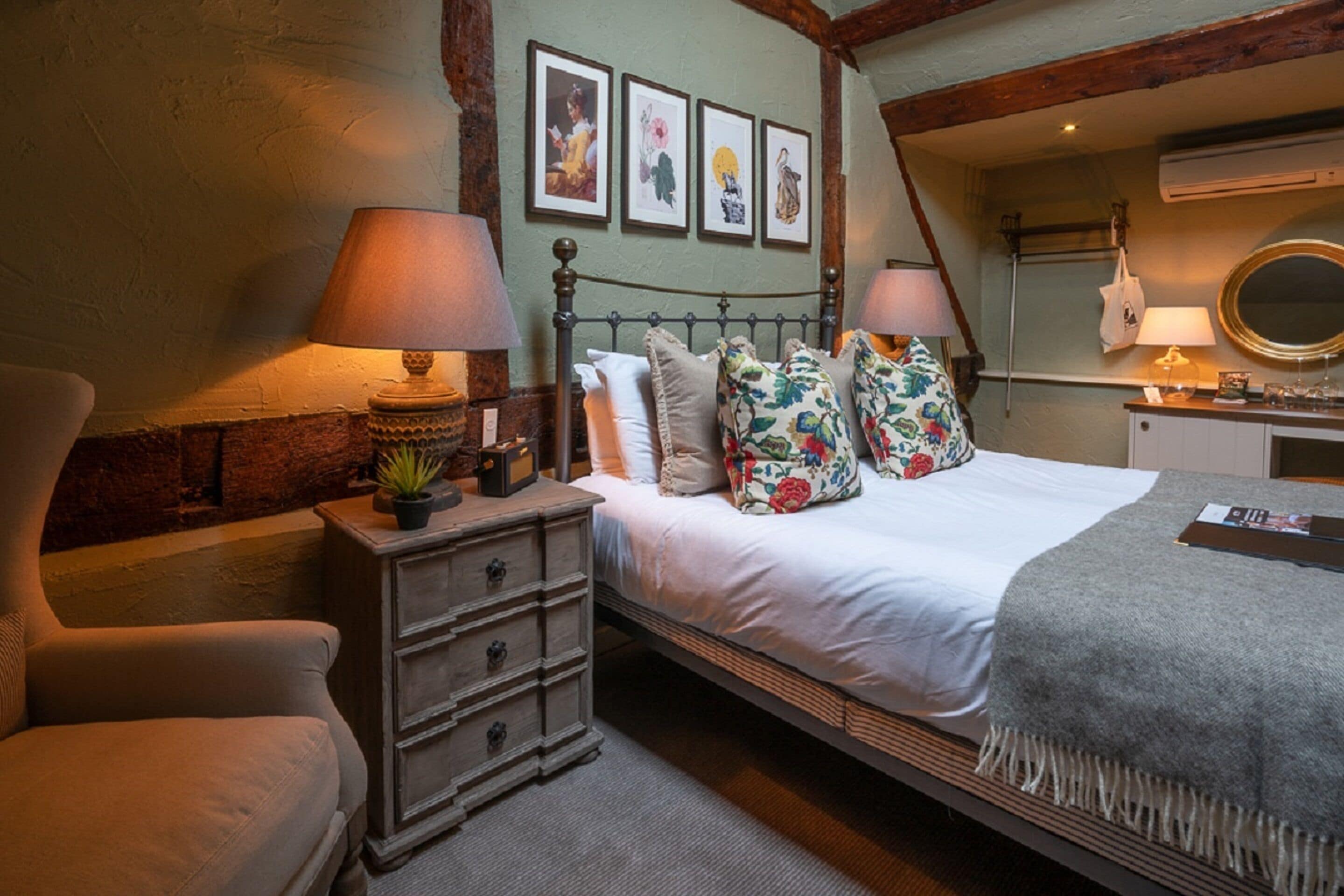 A bedroom with a bed, two bedside tables, a chair, a dresser, a mirror, and framed pictures on the wall.