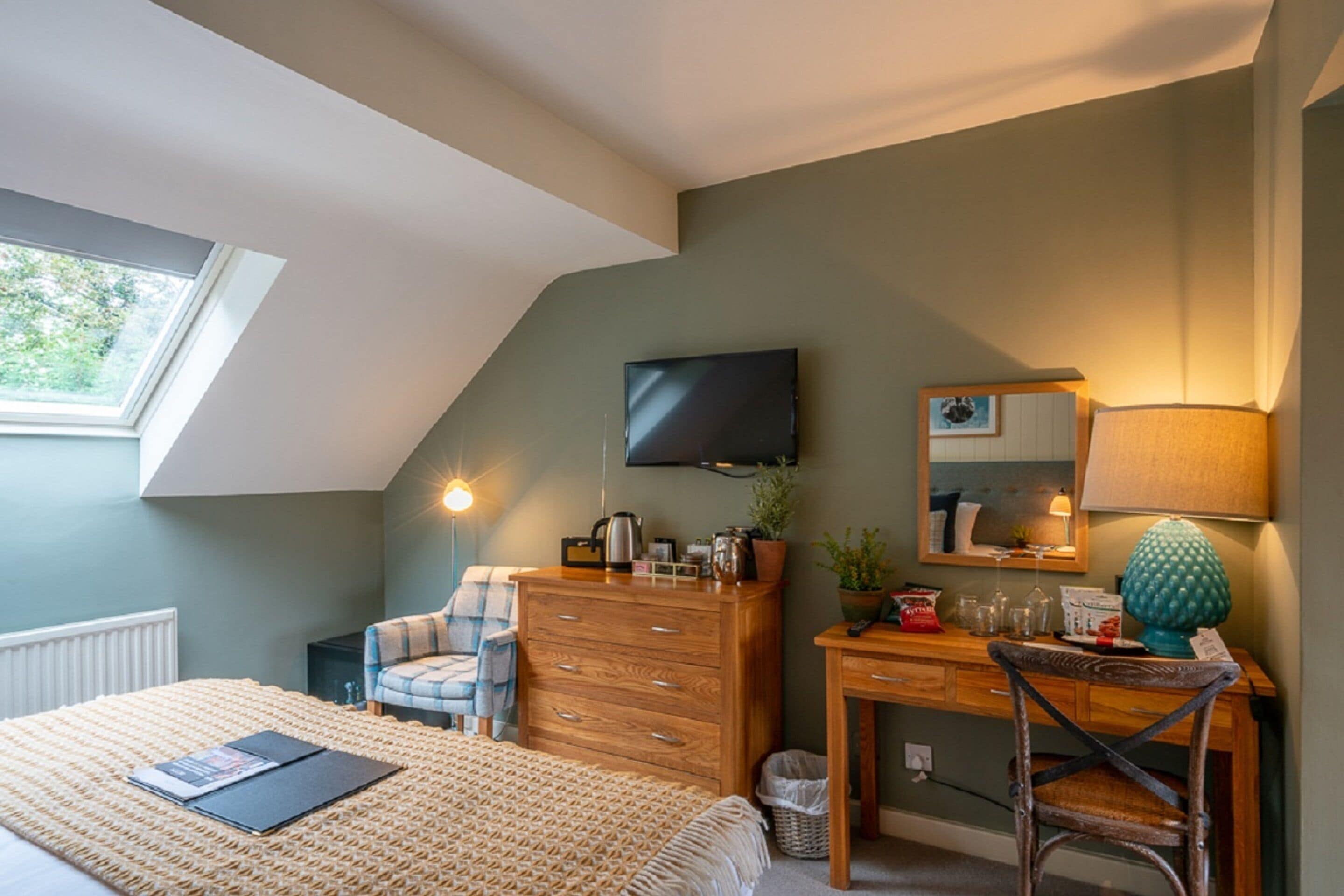 A bedroom with a bed, a desk, a chair, a television, and a window.