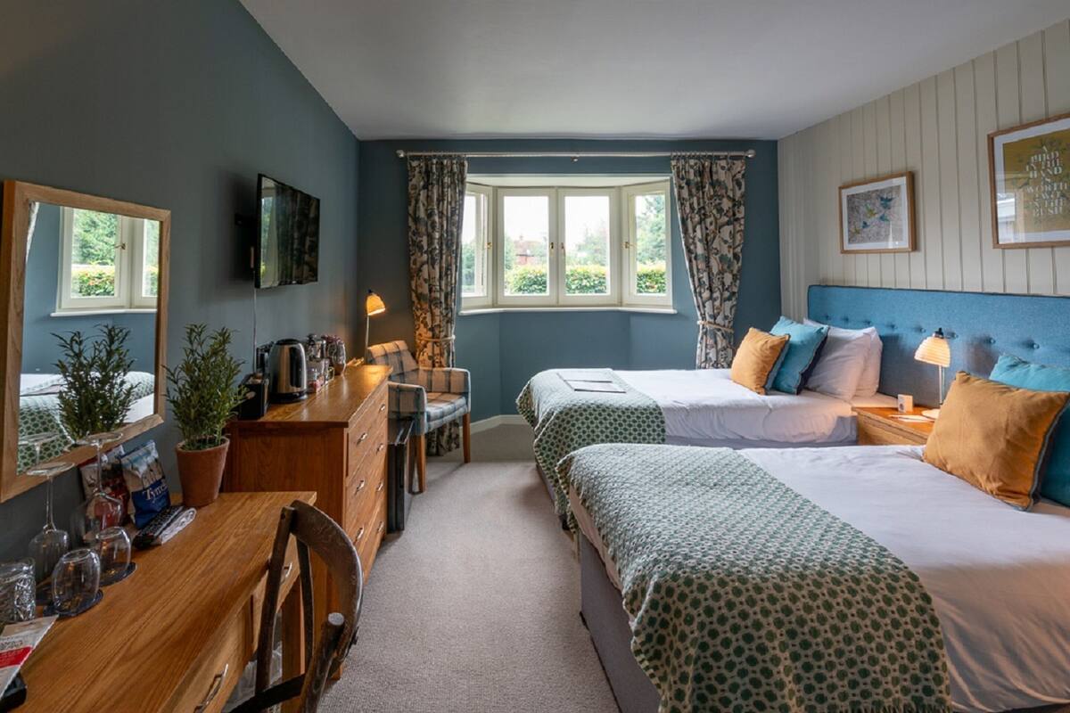 A bedroom with two beds, a desk, a chair, a dresser, a window with curtains, and a television on the wall.