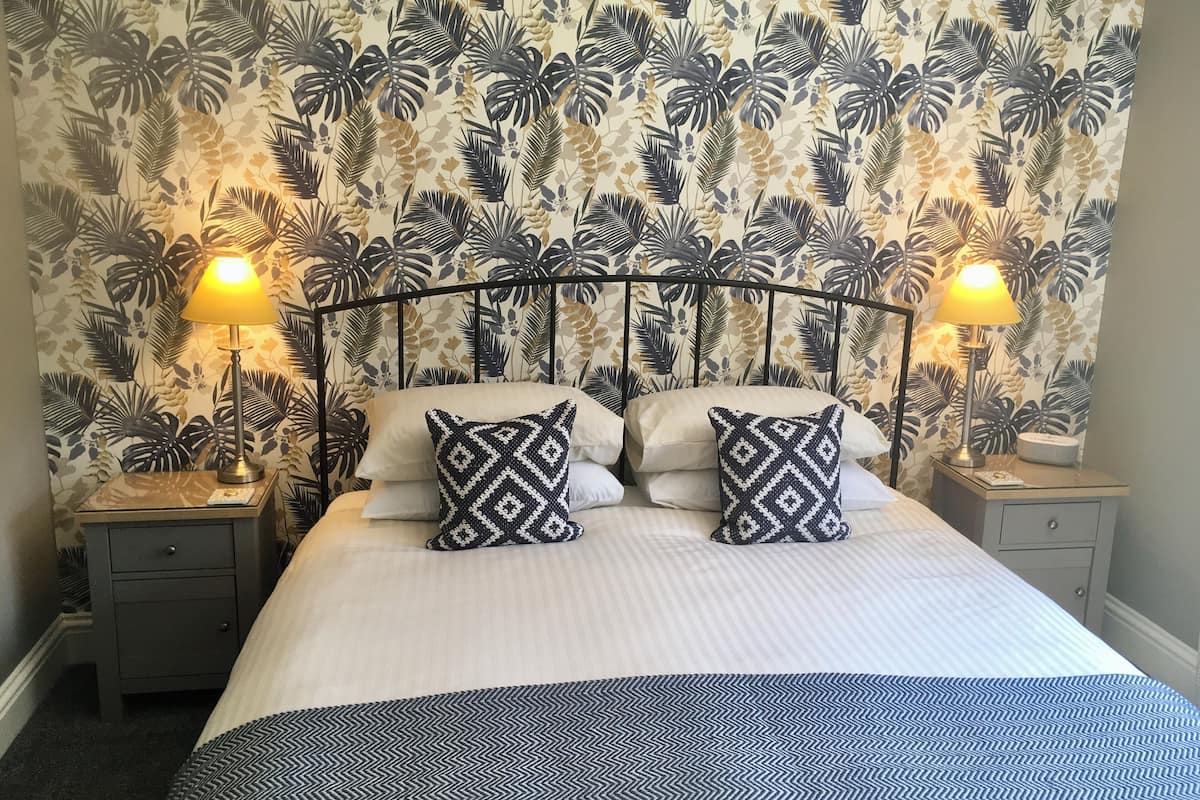 A bed with a patterned bedspread, two decorative pillows, a metal headboard, and two bedside lamps.