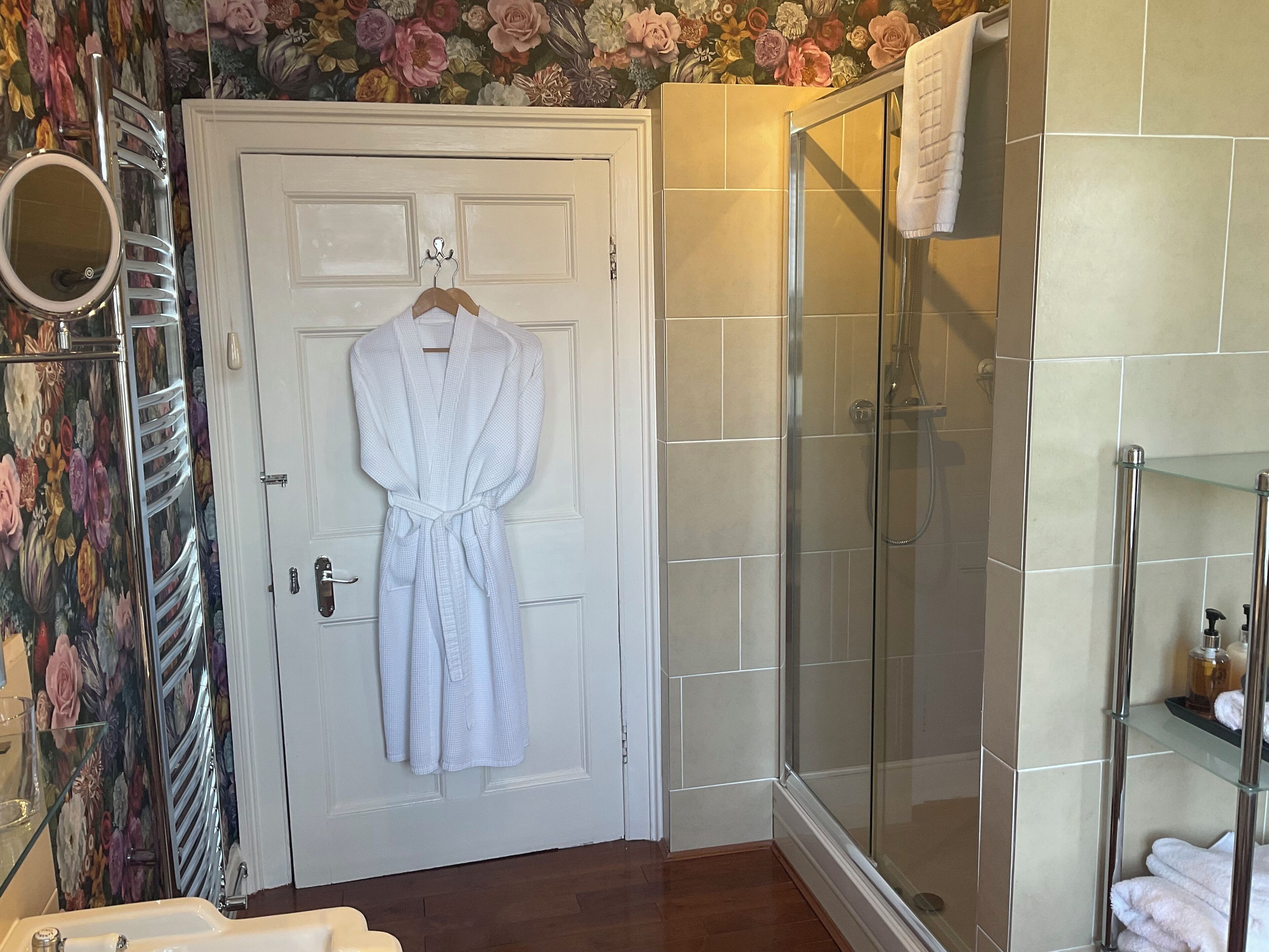 A bathroom with a white door, a glass shower enclosure, and a floral wallpaper design.