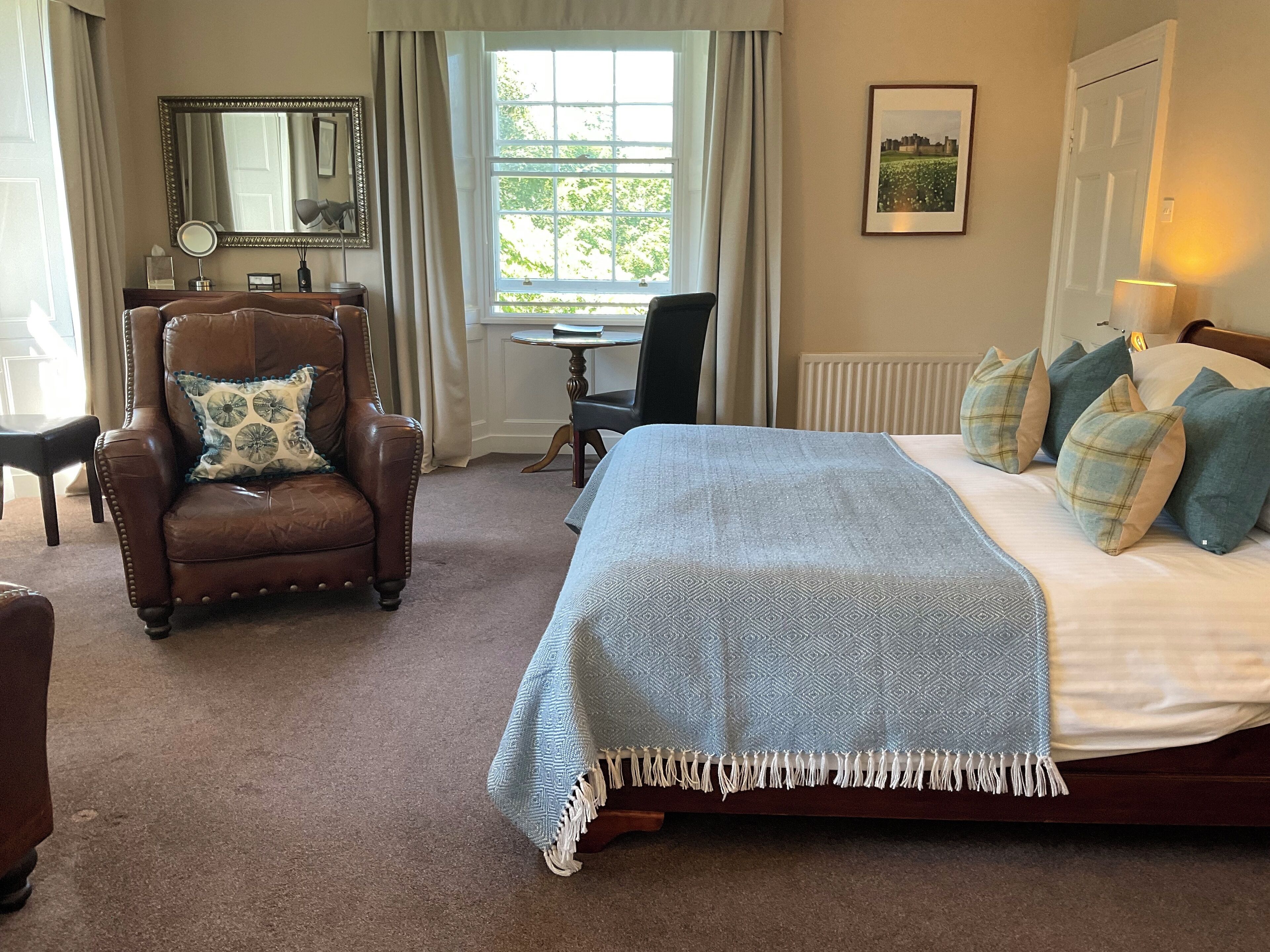 A bedroom with a large bed, a leather armchair, a small table, and a window with curtains.