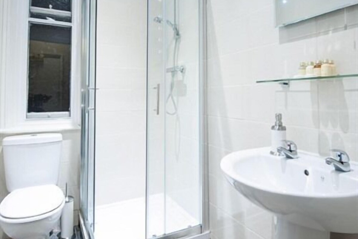A modern bathroom with a glass shower enclosure, a white toilet, and a sink with a glass shelf above it.