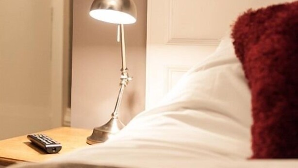 A hotel room with a bed, a nightstand, a lamp, and a remote control.