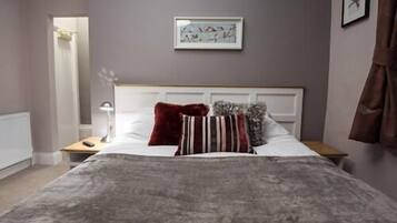 A bedroom with a bed, a nightstand, a lamp, a framed picture on the wall, and a window with curtains.