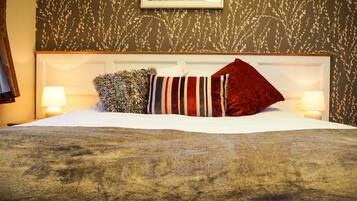 A neatly made bed with a striped pillow, a fluffy pillow, and a red pillow. There are two bedside lamps on either side of the bed.