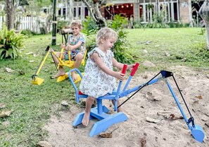 Children playing on outdoor exercise equipment in a garden with a white fence and greenery in the background. - Proud Phu Fah Maerim (Mae Rim)