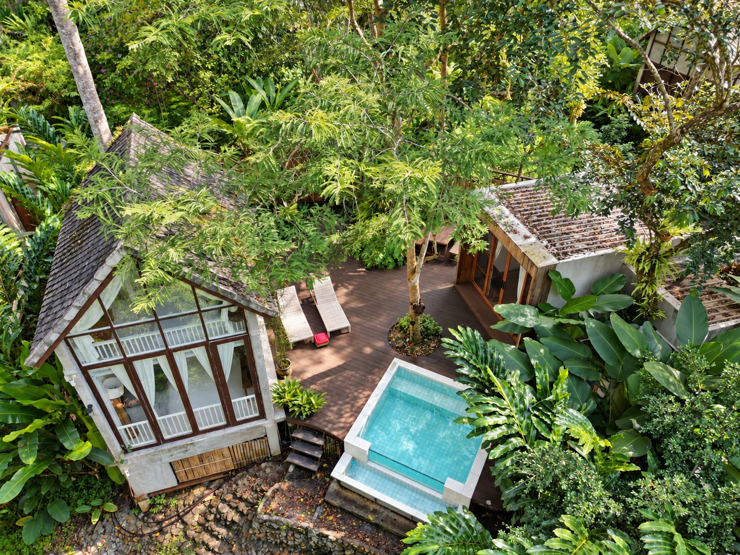 A tropical resort with a swimming pool, wooden deck, and lush greenery.
