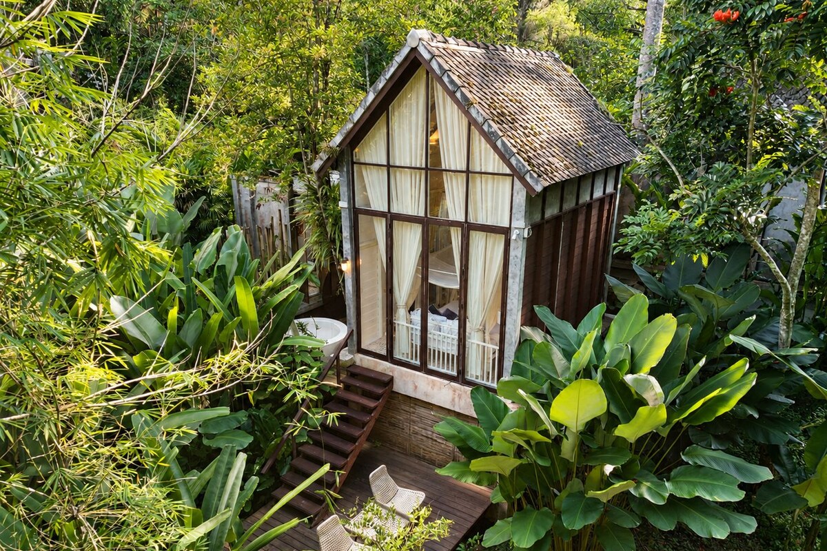 Una pequeña casa de madera con balcón, rodeada de exuberante vegetación.