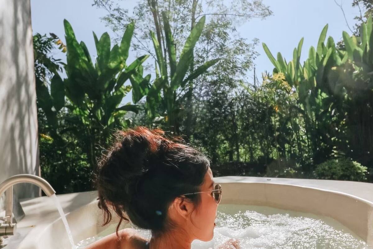 Una persona relajándose en un jacuzzi con vistas a exuberante vegetación y un cielo despejado.