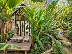 A wooden deck with two chairs and a table, surrounded by lush greenery and a small stream. - Proud Phu Fah Maerim (Mae Rim)