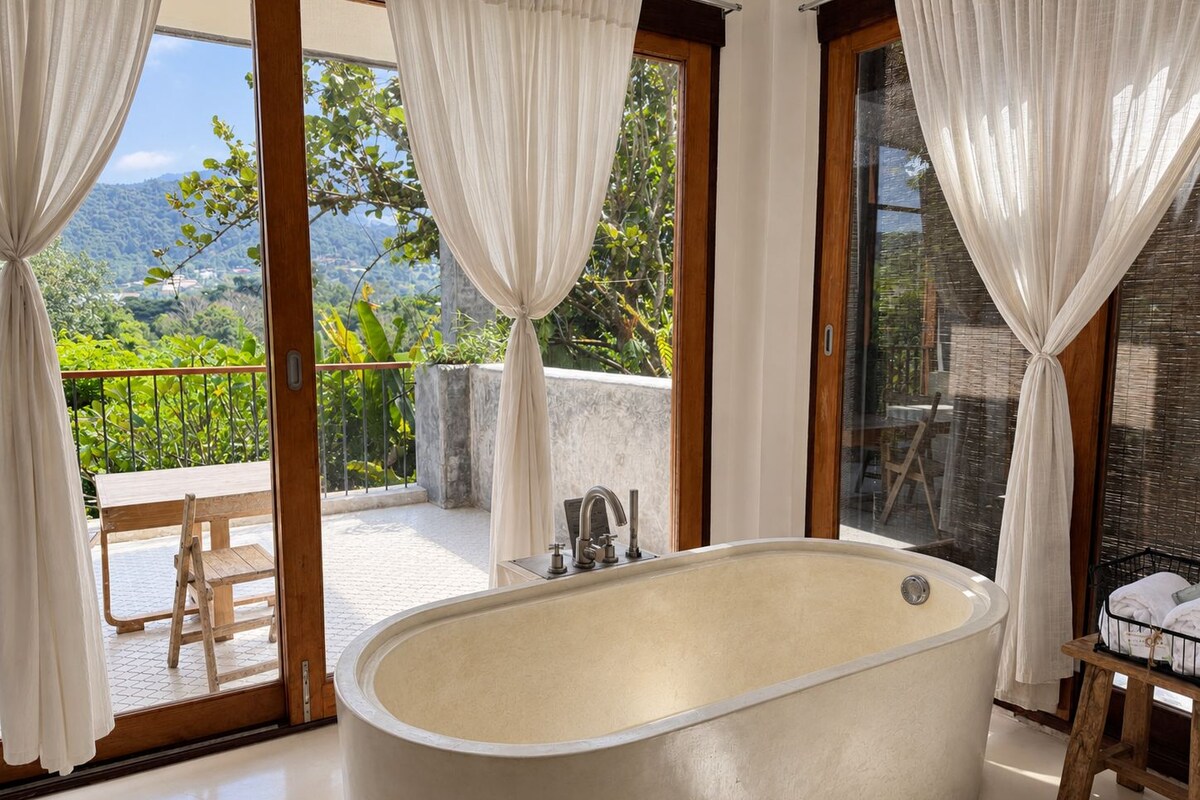 Un baño con una bañera independiente, un banco de madera y vistas a un balcón con mesa y sillas.