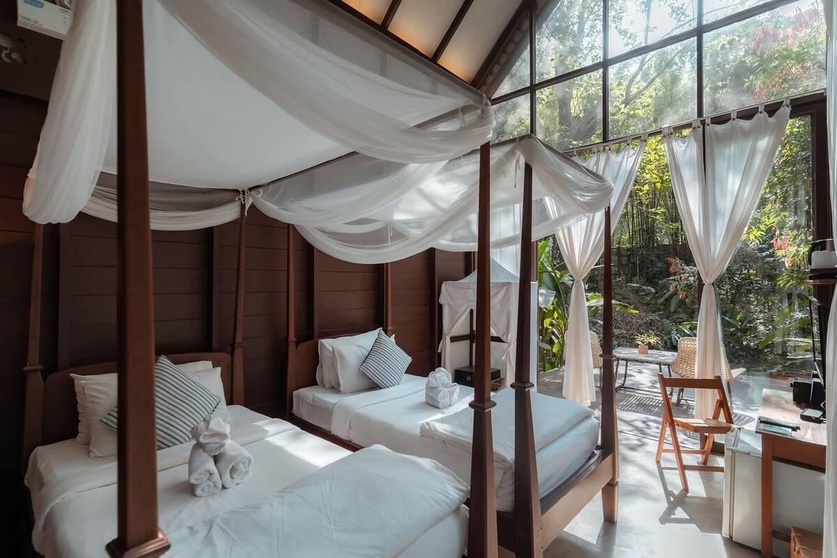 Habitación con tres camas, cada una con ropa de cama blanca y almohadas a rayas, bajo un dosel.