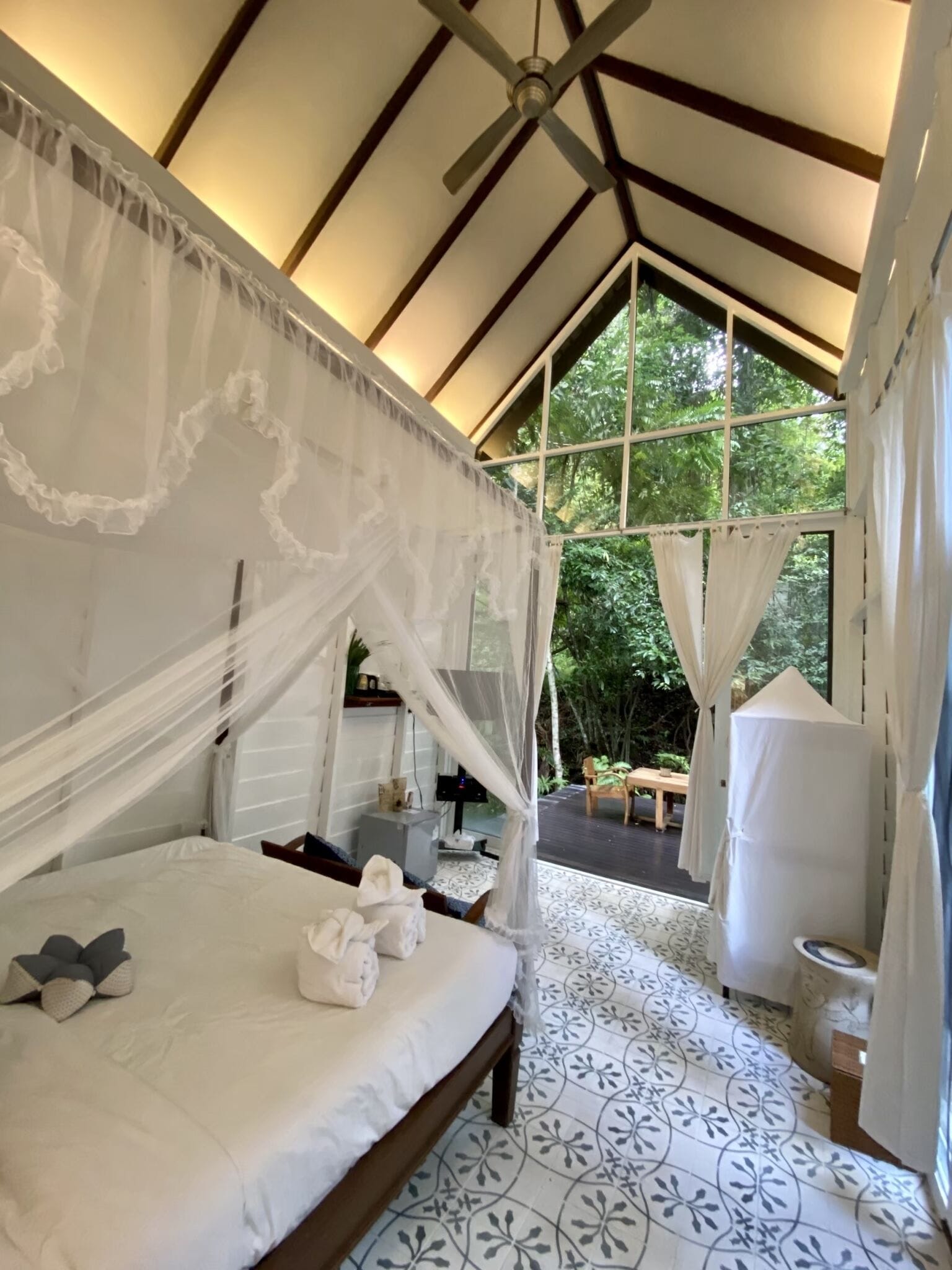 A bedroom with a canopy bed, a TV, a small table, and a view of the outdoors.