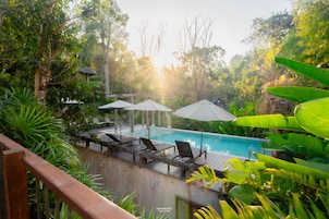A pool area with lounge chairs and umbrellas, surrounded by lush greenery.