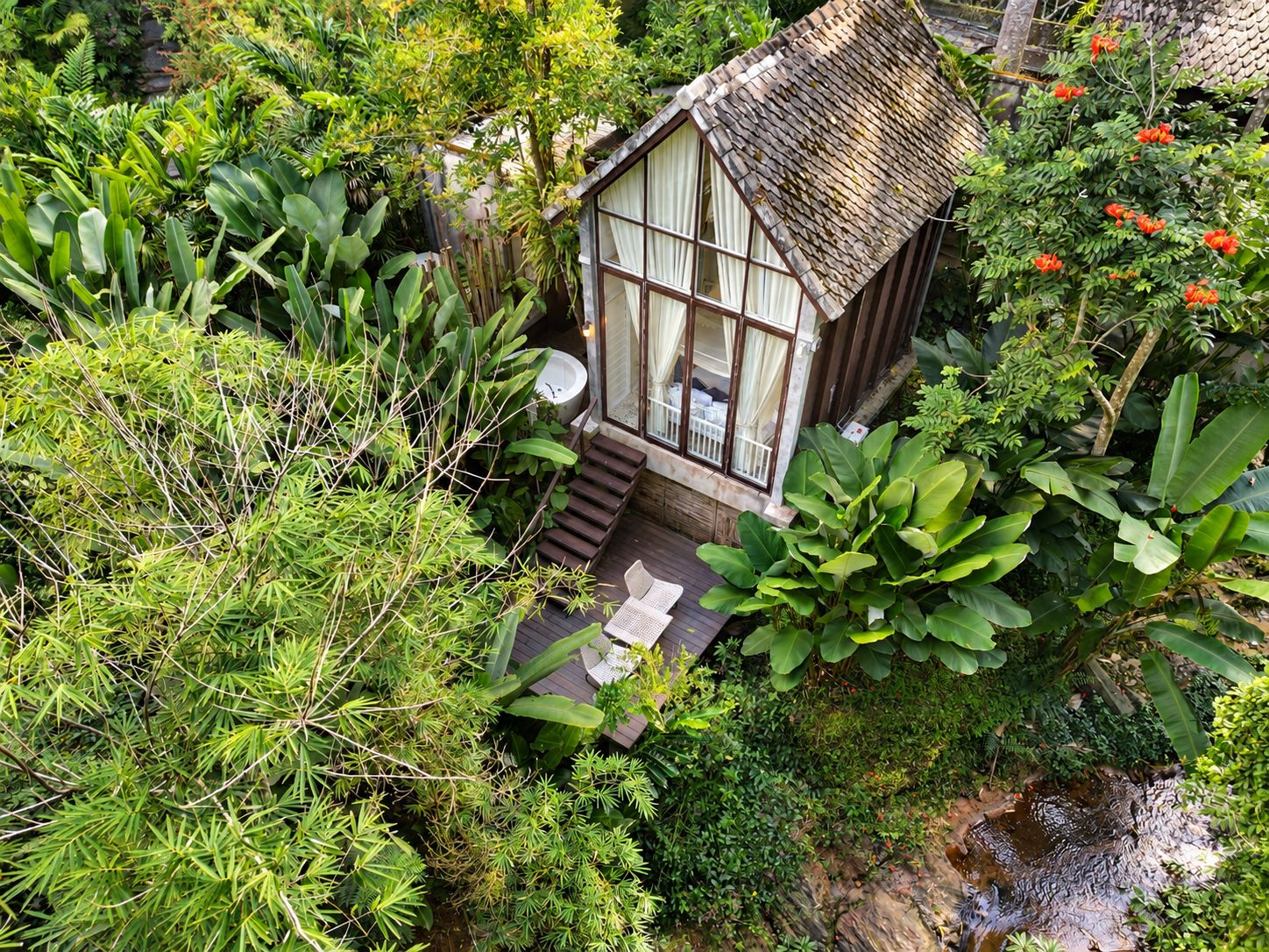 A small, rustic house surrounded by lush greenery and a small stream.