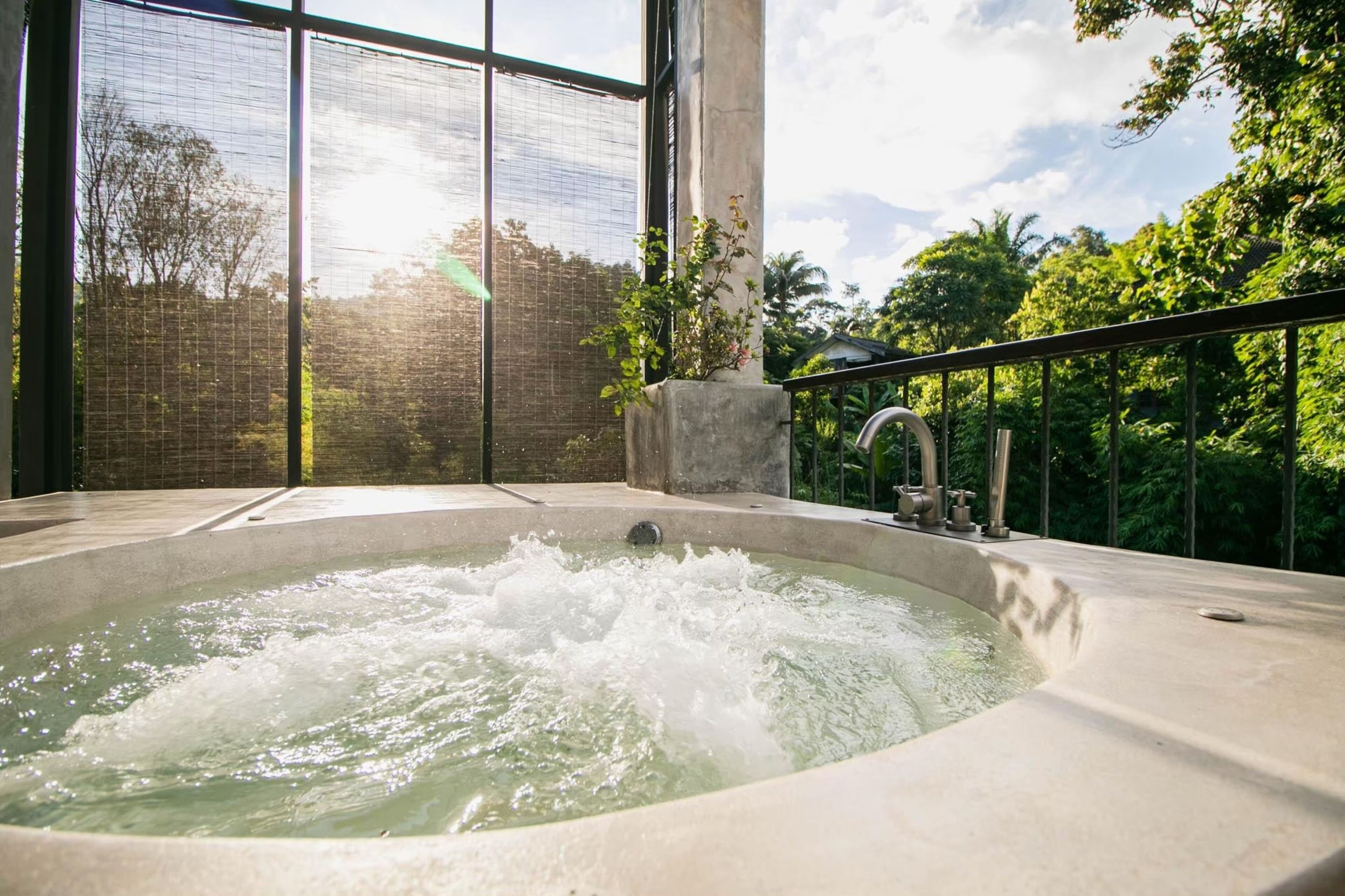 A hot tub with a view of lush greenery and a building in the background.