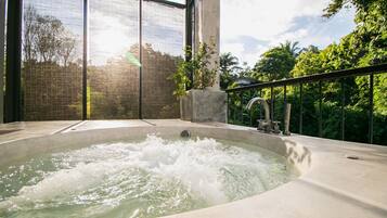 A hot tub with a view of lush greenery and a building in the background.