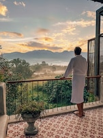 A person standing on a balcony overlooking a mountainous landscape with a view of the sky and clouds.