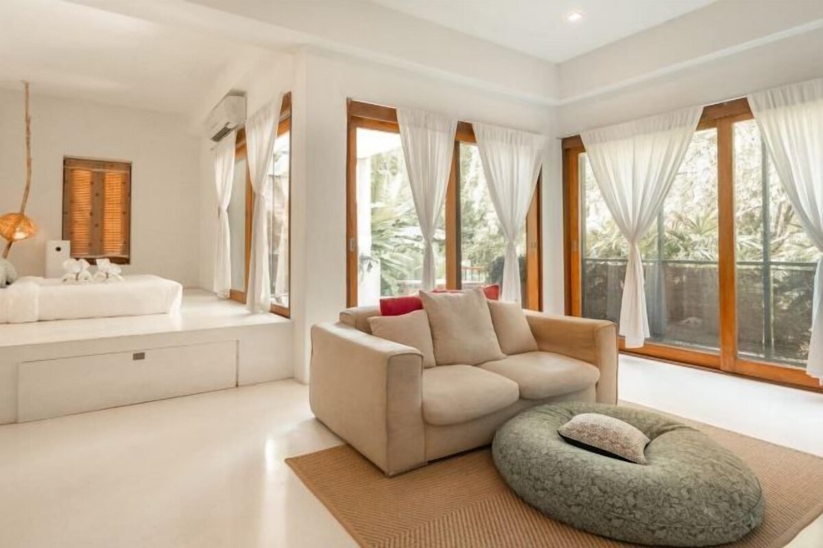 Una sala de estar moderna con un sofá color crema, un sillón de peluche redondo y una mesa de centro blanca.