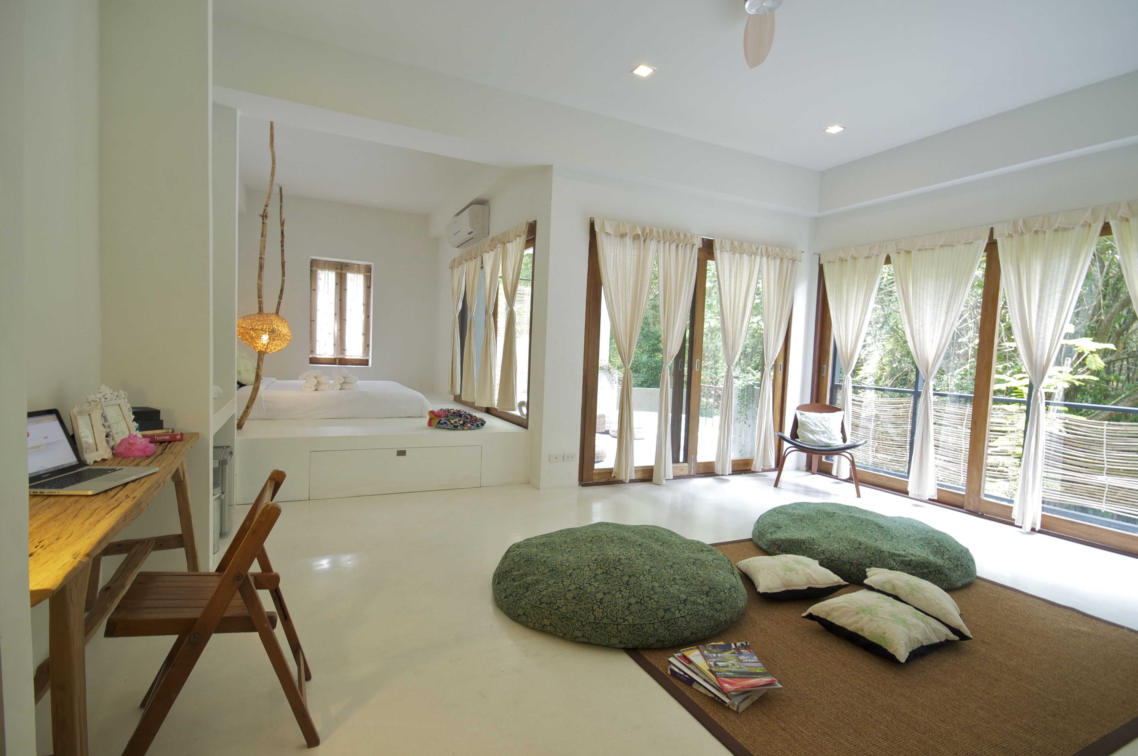 A spacious room with a wooden desk, a green bean bag chair, and a large window with curtains.
