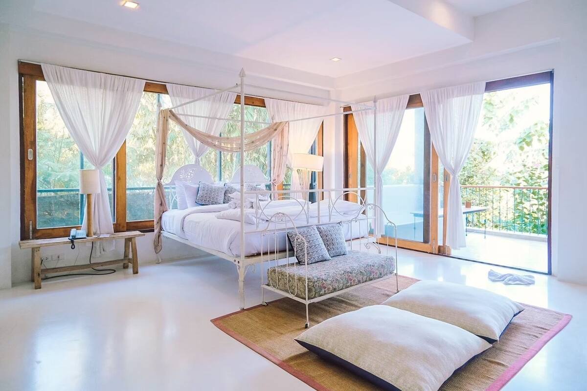 Un dormitorio amplio con cama con dosel, una cama tipo diván y un gran ventanal con vistas a zonas verdes.