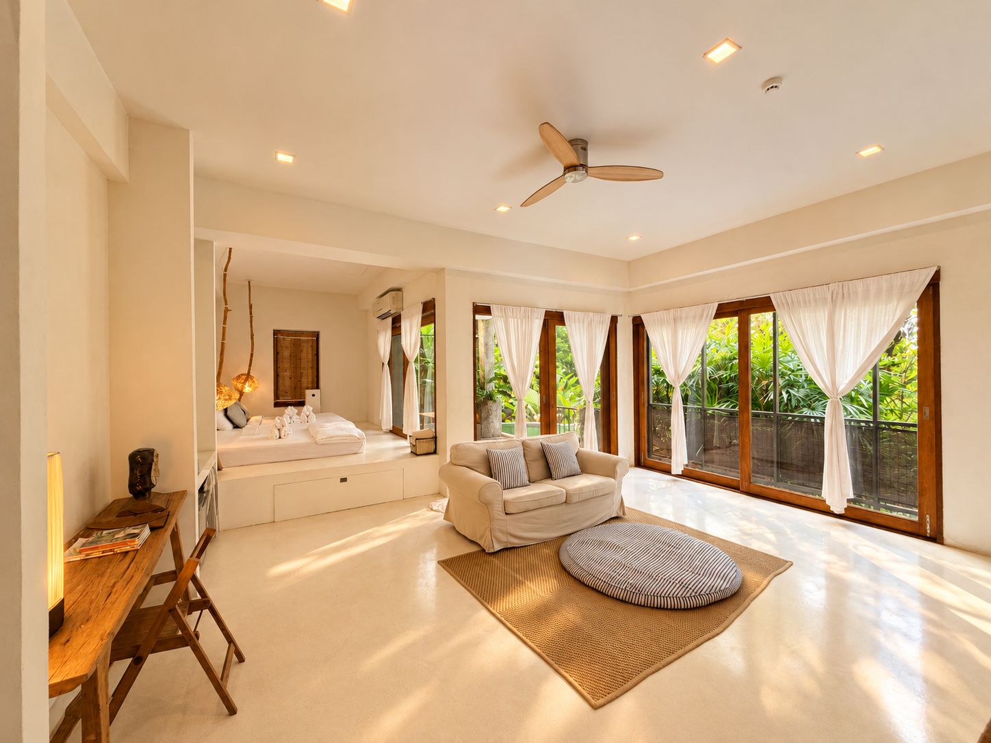 A spacious room with a ceiling fan, large windows with curtains, a sofa, a wooden desk, and a small rug.