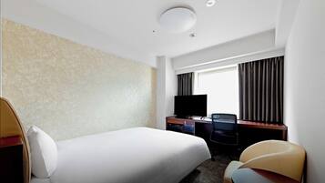 A hotel room with a bed, a desk with a television, a chair, and a window with curtains.